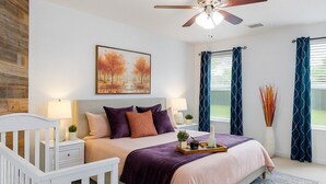 A bedroom with a bed, a crib, a ceiling fan, a painting, and a window with curtains. - Kitchen Foosball Fenced Yard Parking (Kyle)