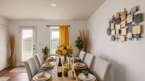 A dining room with a long table set for six, featuring a central vase with yellow flowers, a bottle of wine, and candles. - Kitchen Foosball Fenced Yard Parking (Kyle)