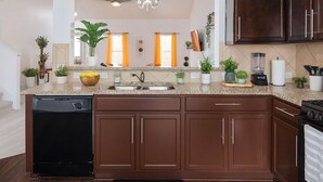 A modern kitchen with dark brown cabinets, a granite countertop, a dishwasher, a stove, and a ceiling light fixture. - Kitchen Foosball Fenced Yard Parking (Kyle)