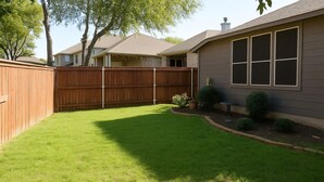 Un jardin avec une clôture en bois, une pelouse et une maison dotée de grandes fenêtres.