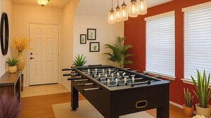 Une pièce avec une table de baby-foot, une porte, un luminaire fixé au mur et plusieurs plantes en pot.