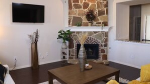 A living room with a stone fireplace, a flat-screen TV mounted on the wall, and a wooden coffee table. - Media Room Pool Table Office Room Kitchen (Wylie)