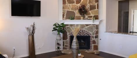 Uma sala de estar com lareira de pedra, televisão de tela plana na parede e mesa de centro de madeira.