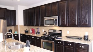 A modern kitchen with dark wood cabinets, stainless steel appliances, granite countertops, and a built-in microwave. - Media Room Pool Table Office Room Kitchen (Wylie)