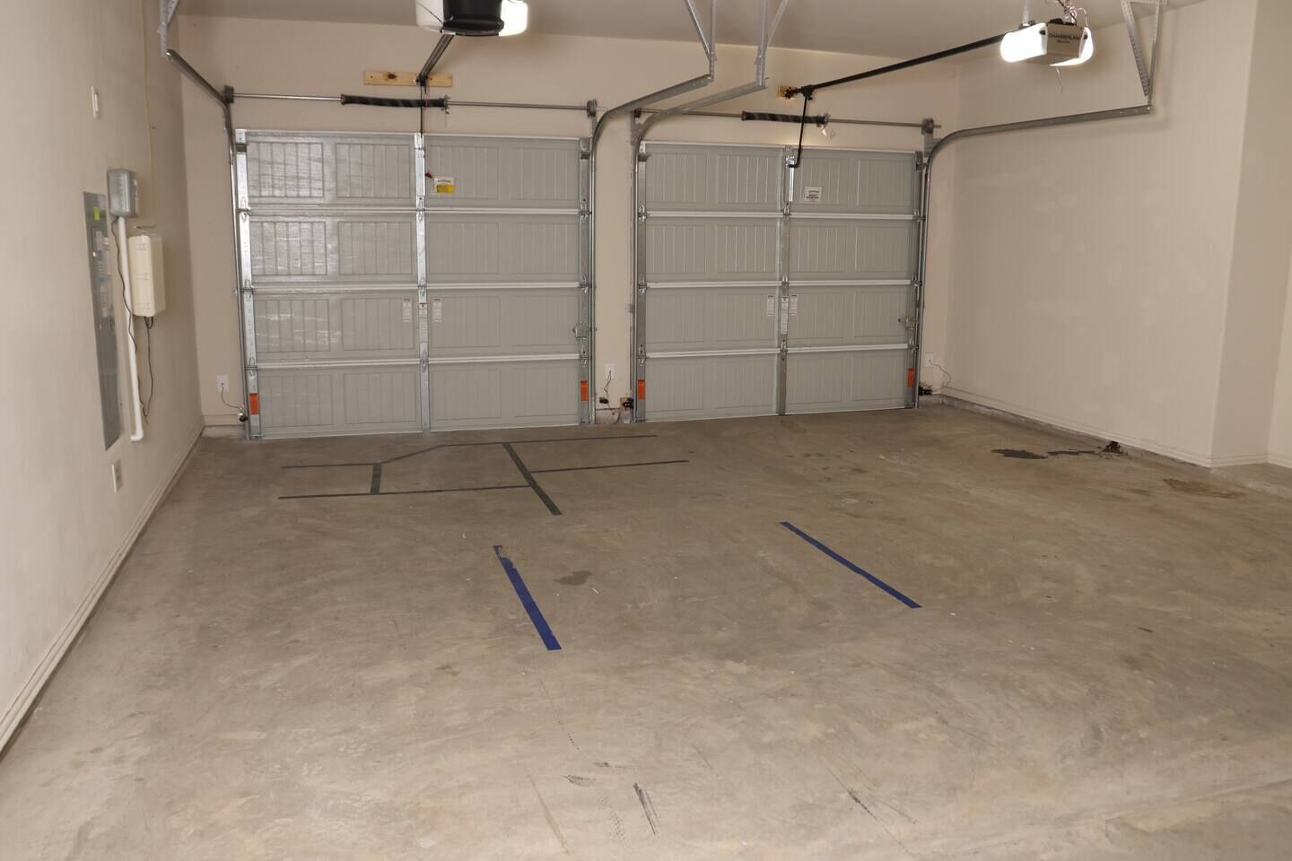 A garage with two closed garage doors, a concrete floor, and visible electrical conduits.