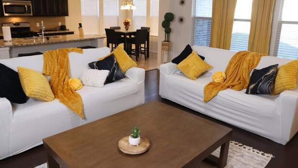 A modern living room with two white sofas, a wooden coffee table, and a dining area in the background. - Media Room Pool Table Office Room Kitchen (Wylie)