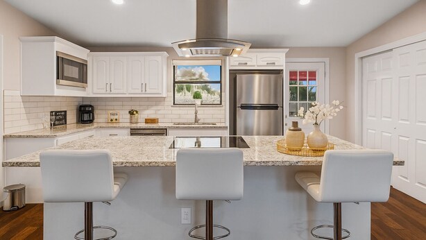 Une cuisine moderne avec des meubles blancs, un réfrigérateur en acier inoxydable, un four encastré et un grand îlot central doté de tabourets de bar.