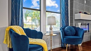 Un salon moderne avec deux fauteuils bleus, un plaid jaune, une lampe sur pied et une vue sur l’extérieur grâce à de grandes fenêtres.