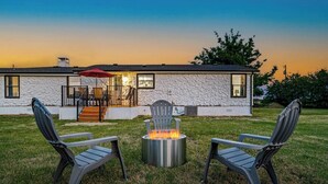 Une maison moderne avec une façade en pierre, un patio agrémenté de deux fauteuils Adirondack et un foyer au centre.