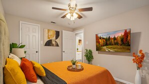 Une chambre à coucher avec un lit, un ventilateur de plafond, un tableau, une télévision et un vase rempli de fleurs.