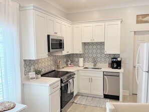A modern kitchen with white cabinetry, a built-in microwave, a coffee maker, and a dishwasher. - The Nest at Circle Park - Cute Cozy Cottage (St. Simons Island)