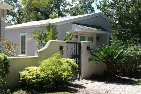 A house with a gated entrance, surrounded by various plants and trees. - The Nest at Circle Park - Cute Cozy Cottage (St. Simons Island)