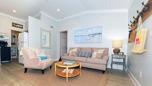 Un salon avec un canapé beige, un fauteuil rose, une table basse et un tableau accroché au mur.