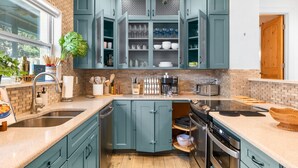 Een moderne keuken met blauwgroene kastjes, een centraal eiland en een achterwand van baksteen.