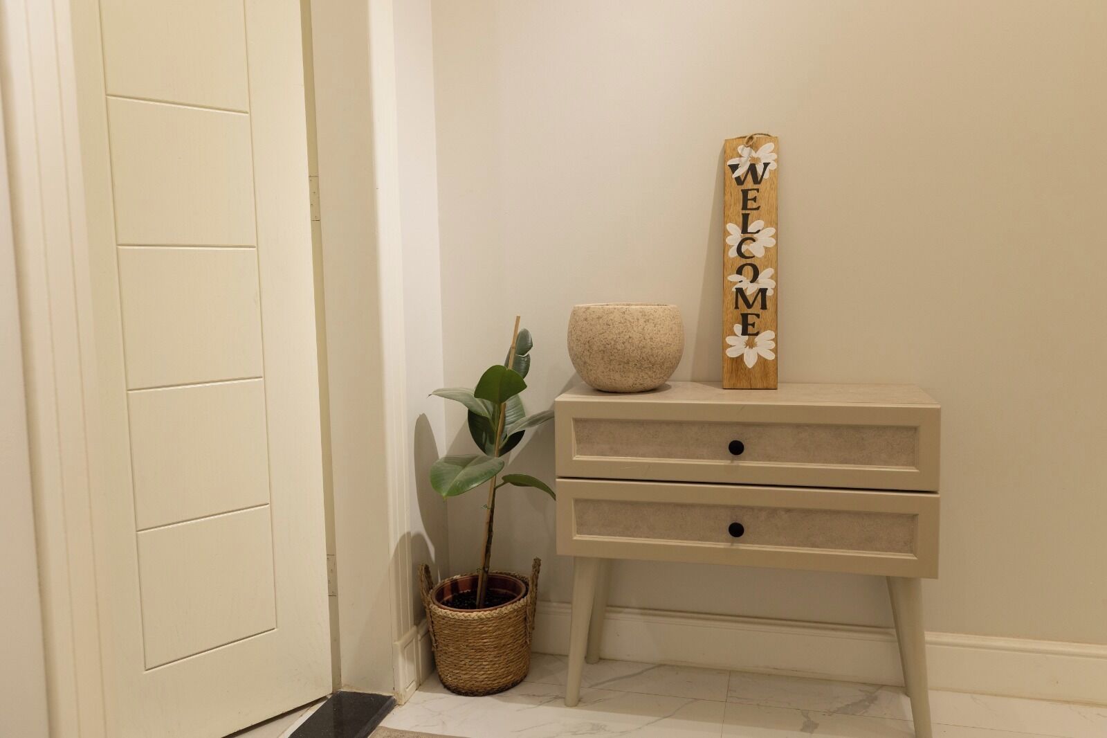 A hallway with a wooden welcome sign, a potted plant, and a wicker basket.