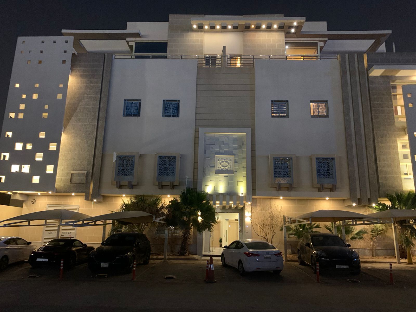Un hotel moderno con una fachada simétrica, varios balcones y un estacionamiento con varios coches.