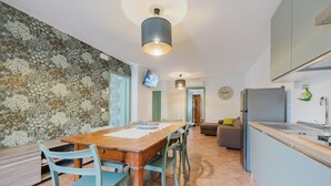A modern kitchen with a wooden dining table, blue chairs, and a TV mounted on the wall.