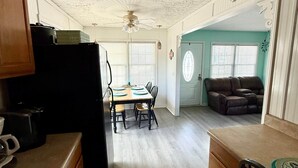 A kitchen with a dining area, a ceiling fan, and a view into a living room with a couch and a door. - 5327 Ocean Lakes Pet Friendly Golf Cart⛱️🏝️🩱🌊👙☀️🐚 (Myrtle Beach)