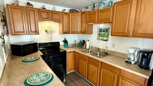A kitchen with wooden cabinets, a microwave, stove, and a coffee maker. - 5327 Ocean Lakes Pet Friendly Golf Cart⛱️🏝️🩱🌊👙☀️🐚 (Myrtle Beach)