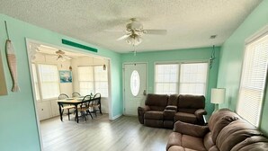 A spacious living room with a brown leather couch, a dining area with a table and chairs, and a ceiling fan. - 5327 Ocean Lakes Pet Friendly Golf Cart⛱️🏝️🩱🌊👙☀️🐚 (Myrtle Beach)