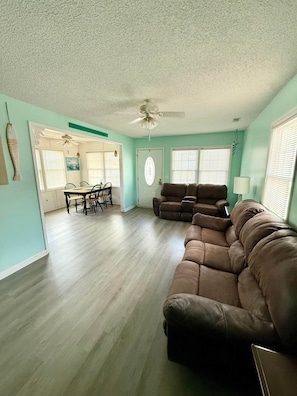 A spacious living room with a brown leather couch, a dining area with a table and chairs, and a ceiling fan.