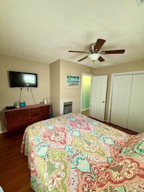 Un dormitorio con cama, cómoda, televisor, ventilador de techo y una puerta.