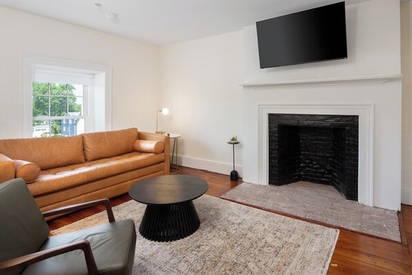 A living room with a leather sofa, a round coffee table, a fireplace, and a flat-screen TV mounted above it.