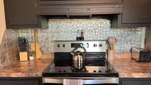 A kitchen with a stainless steel stove, a kettle, and a toaster. There are cabinets, a countertop, and a backsplash with a geometric pattern. - No cleanup chores-Fenced yard, fire pit. Close to I81, downtown. Walk to casino. (Bristol)