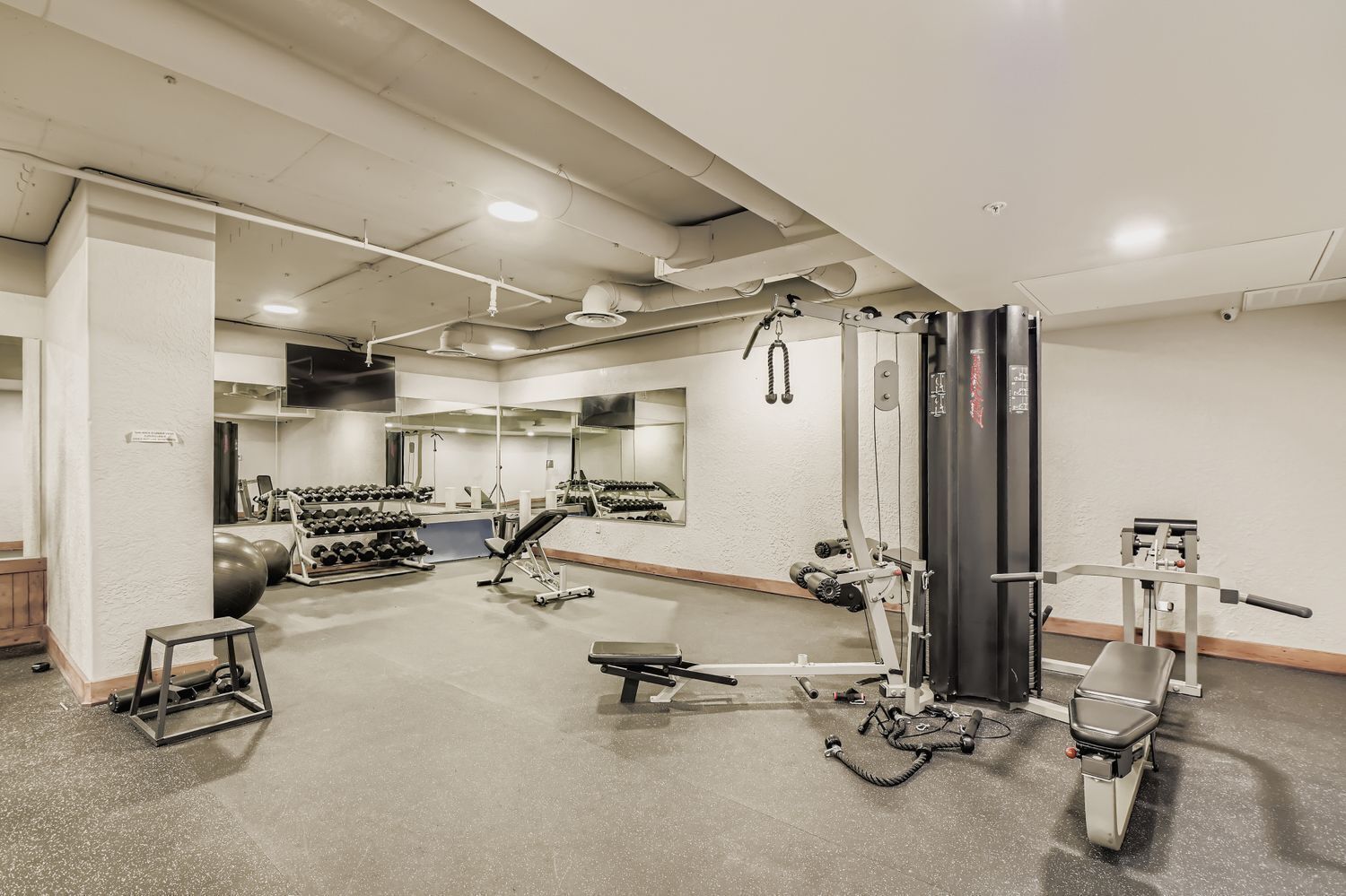 A gym with exercise equipment, mirrors, and a weight rack.
