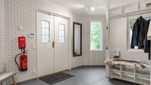 A room with a white door, a fire extinguisher, a bench, and a window with a view of trees.