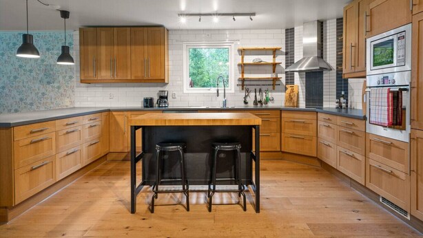 A modern kitchen with wooden cabinets, a central island with stools, stainless steel appliances, and pendant lighting.