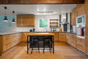 A modern kitchen with wooden cabinets, a central island with stools, stainless steel appliances, and pendant lighting. - Family Friendly Villa near the Water (Södermanlands län)
