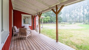 A covered porch with wooden flooring, a table and chairs, and a view of a grassy yard.
