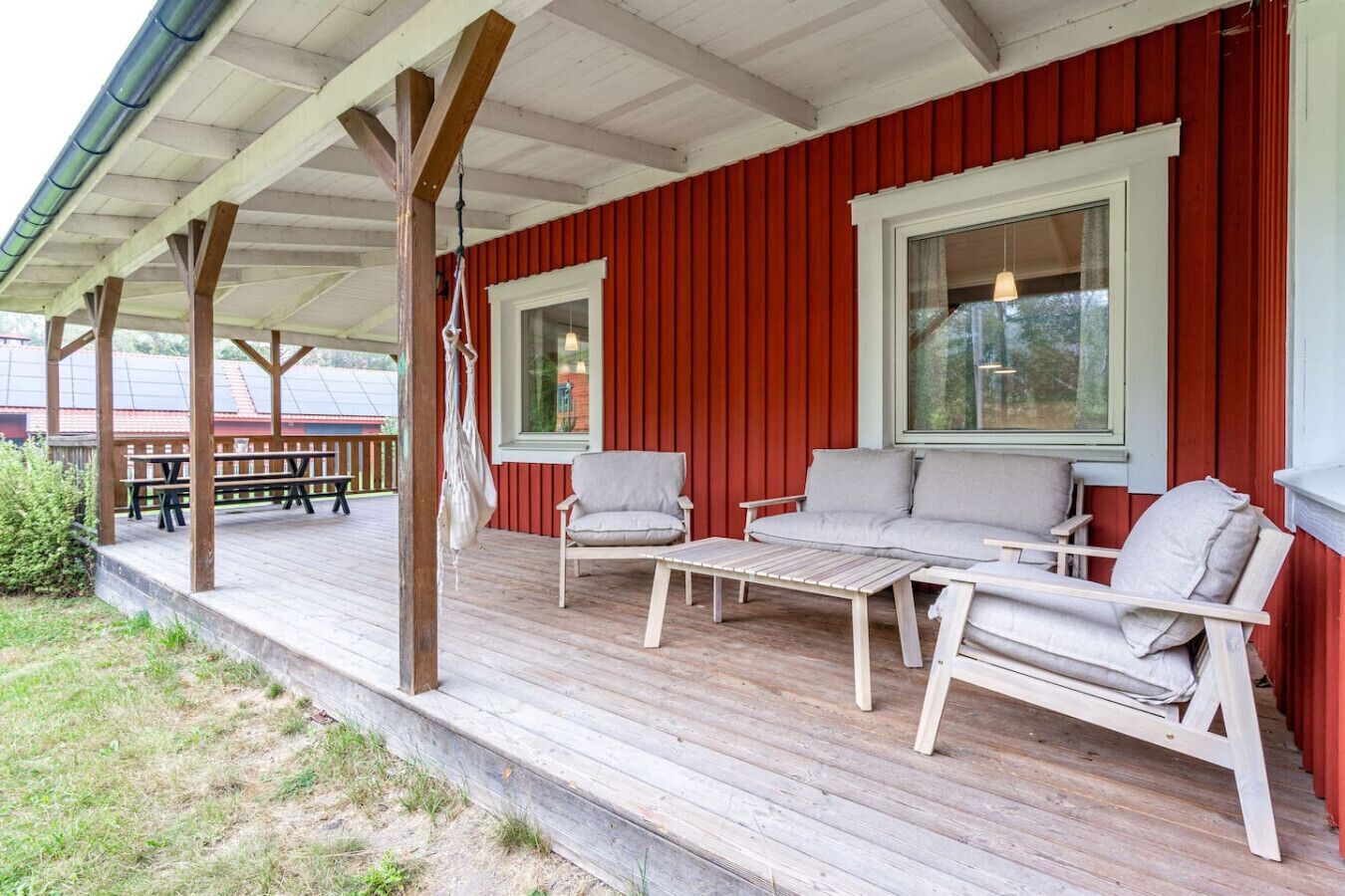 Zona relax all'aperto coperta, con mobili in legno e una parete rossa.