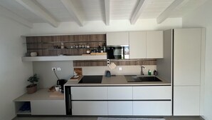 A modern kitchen with white cabinetry, a built-in oven, and a microwave. There is a wooden shelf above the sink and a potted plant on the counter. - Villa Sisine, 🏊 Private pool, Just a 5-Minute Walk from the Beach (Sardegna)