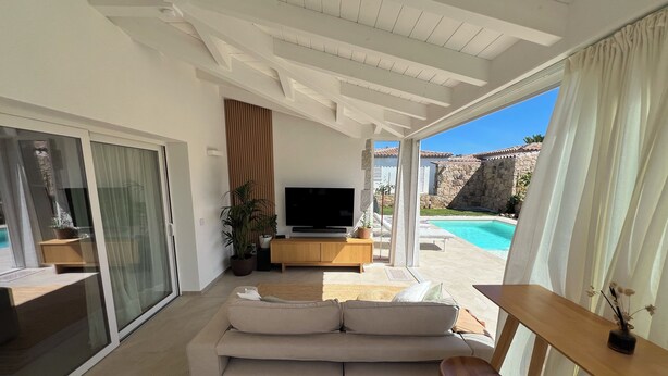 A modern living room with a sofa, TV, and a view of a swimming pool. - Villa Sisine, 🏊 Private pool, Just a 5-Minute Walk from the Beach (Sardegna)