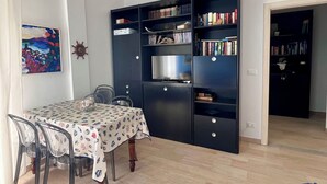 Ein kompakter Wohnraum mit Essbereich, einer eingebauten Bücherreol und einer Küchenzeile.