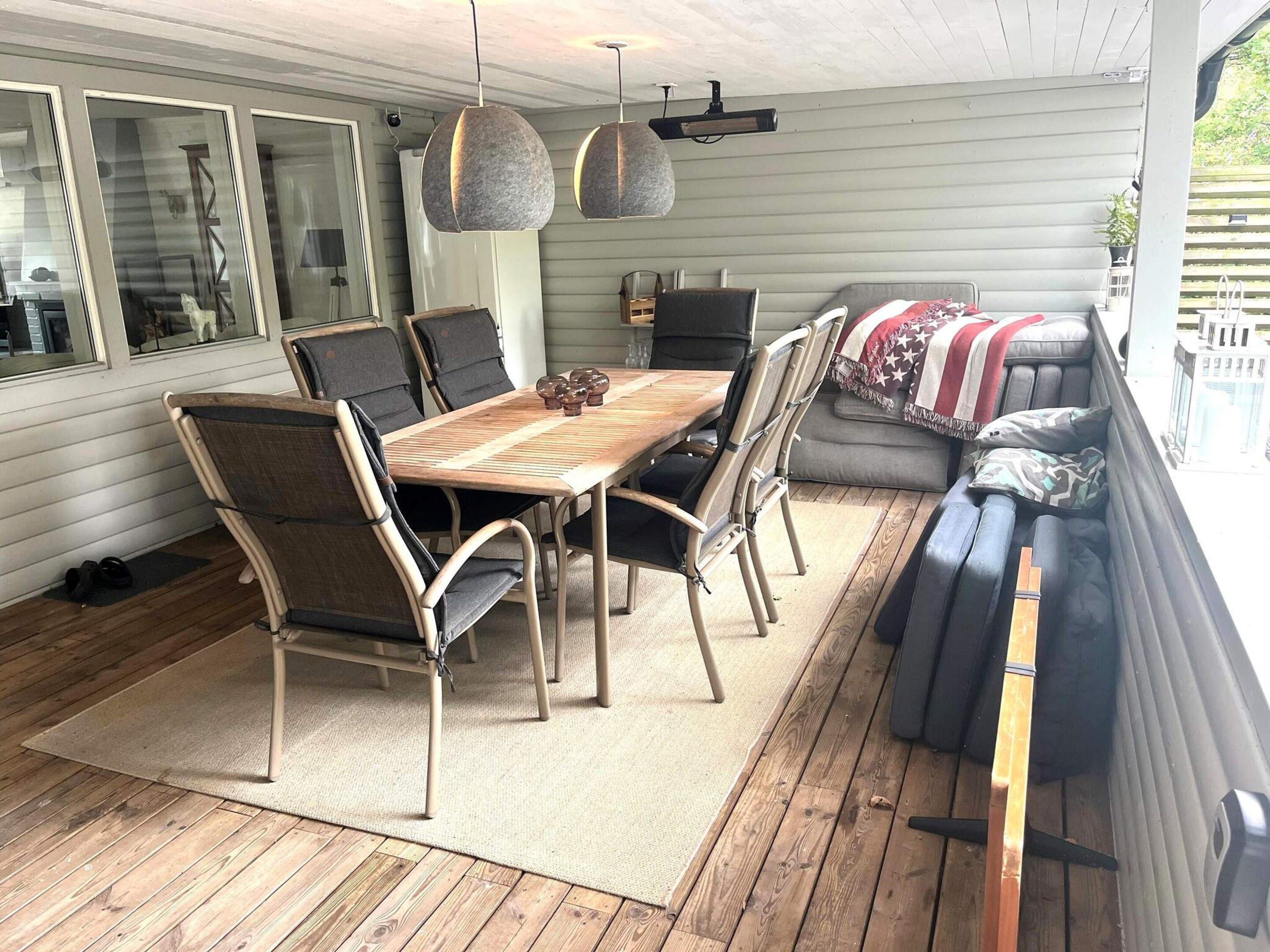 Une terrasse couverte avec une table et des chaises en bois, un canapé et un ventilateur de plafond.
