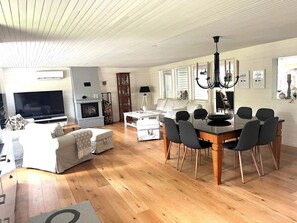A modern living room with a fireplace, a dining area with a glass table, and a television in the corner.