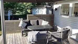 Eine Holzterrasse mit Tisch und Stühlen, einem überdachten Sitzbereich und einem Holzzaun.