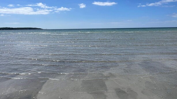 Ein Strand mit klarem Wasser und einer entfernten Landmasse.