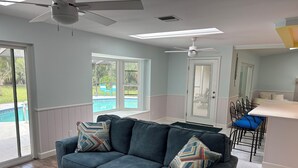 A living room with a dark blue sofa, a remote control on a small table, and a view of a pool through large windows.