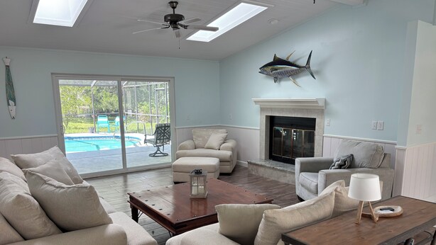 A spacious living room with a fireplace, a ceiling fan, and a view of a swimming pool.