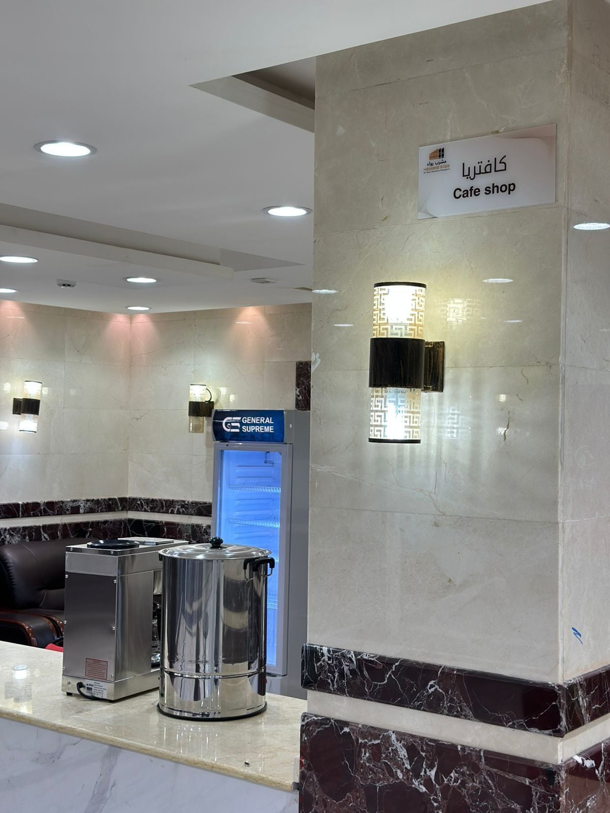 A cafe area with a marble counter, a coffee machine, a General Supreme coffee machine, and a wall-mounted light fixture.