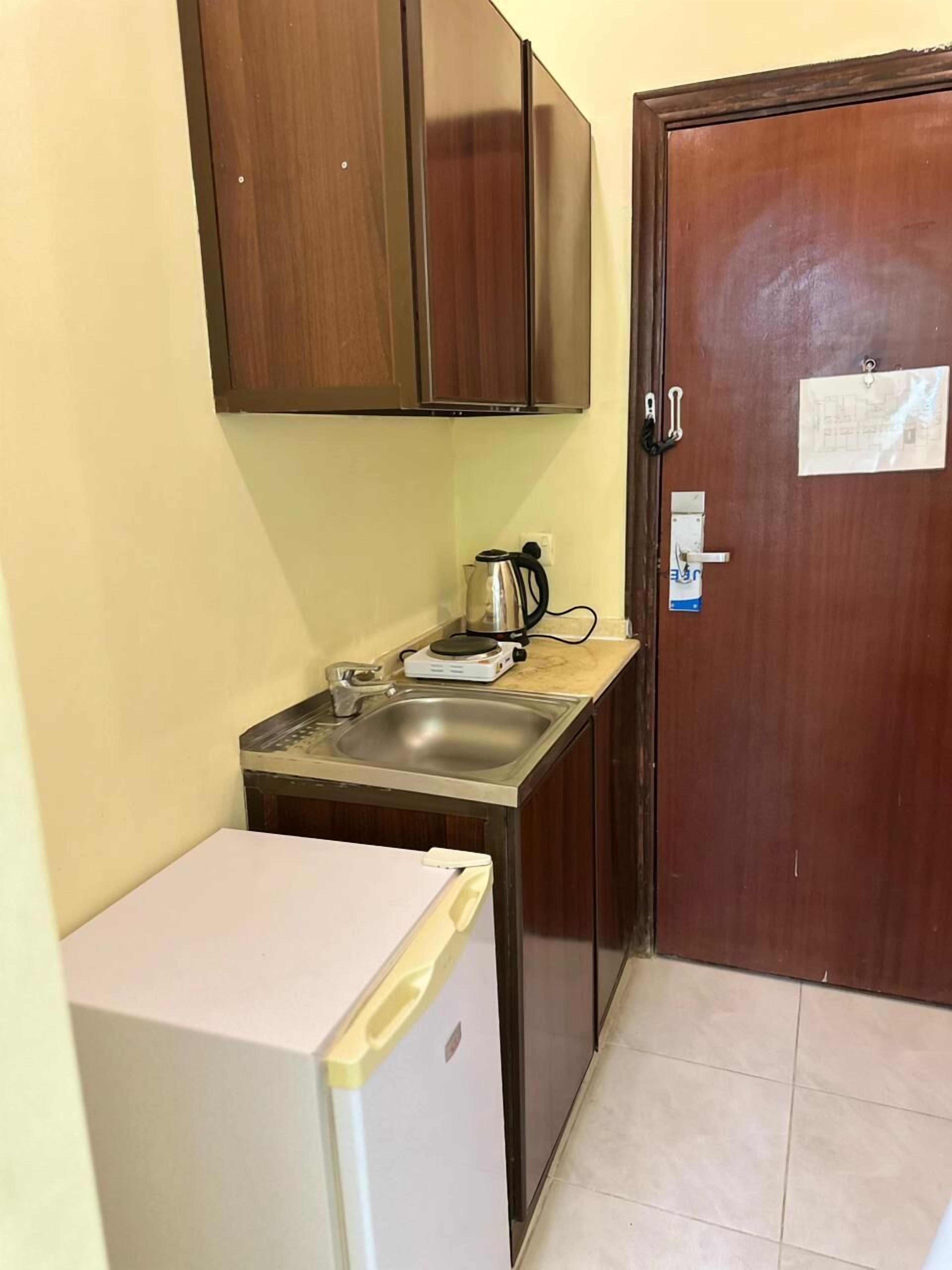 Una cocina compacta con un refrigerador, un lavamanos y una tetera sobre la encimera.