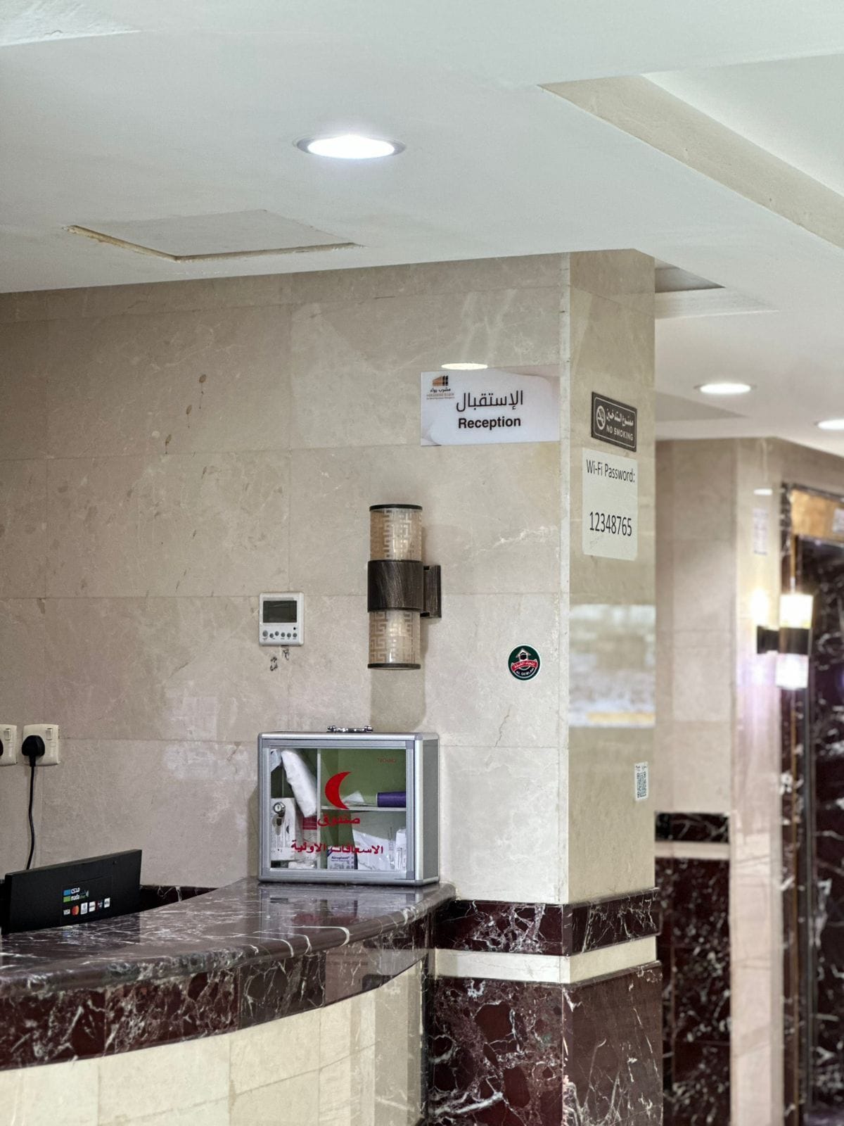 A reception area with a marble counter, a digital screen, a Wi-Fi password sign, and a no-smoking sign.