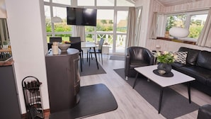 A modern living room with a sofa, a coffee table, a TV, and a dining area with chairs and a table. - 4 Star Holiday Home in Friedrichkoog (Friedrichskoog)
