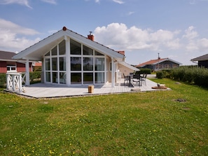 Una casa moderna con un amplio ventanal, un porche cubierto y una terraza.