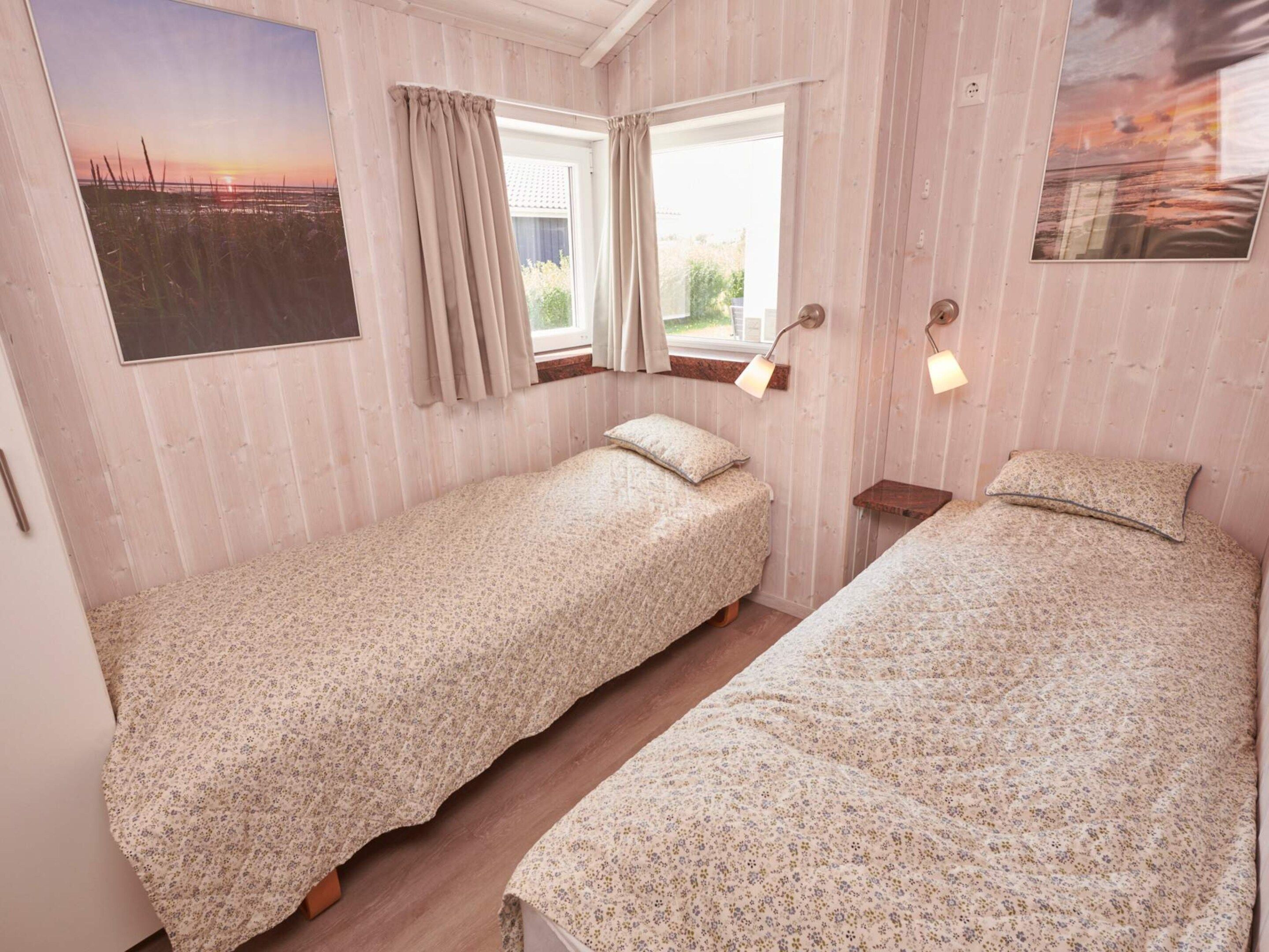 Une chambre avec deux lits simples, une fenêtre avec des rideaux, une lampe fixée au mur et un tableau.