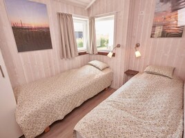 Ein Zimmer mit zwei Einzelbetten, einem Vorhangfenster, einer Wandlampe und einem Gemälde.